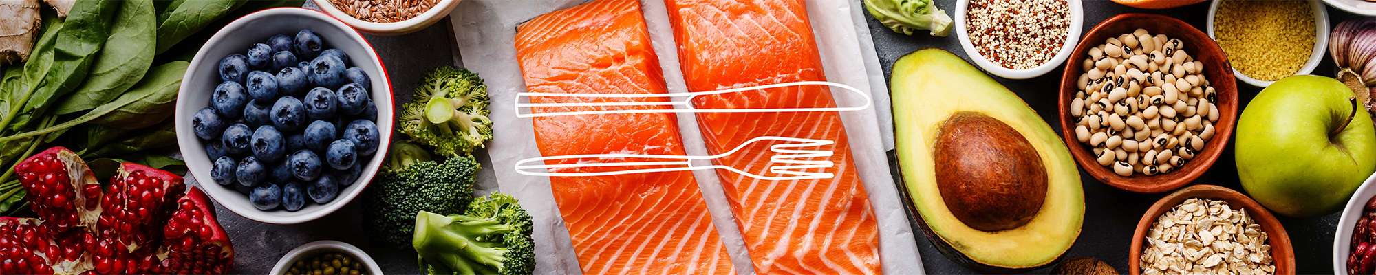 Lebensmittel wie Lachsfilet, frisches Obst und Gemüse sowie Bohnen auf einer Steinplatte